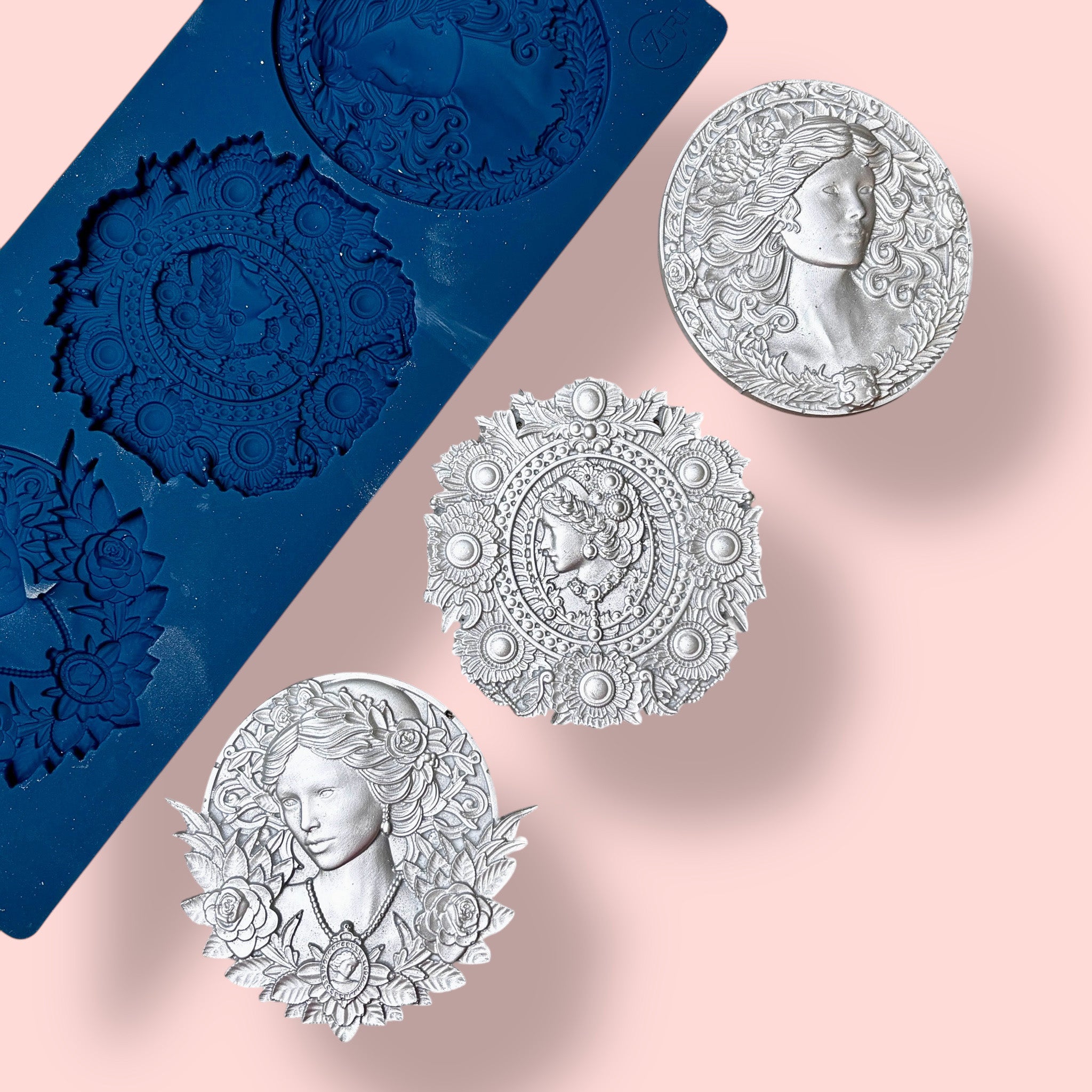 A blue silicone mold and silver colored castings of 3 ornate cameo medallions are against a light pink background.