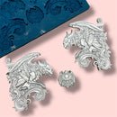 A blue silicone mold and silver colored castings featuring 2 large gargoyle statues and a smaller gargoyle medallion are against a light pink background.