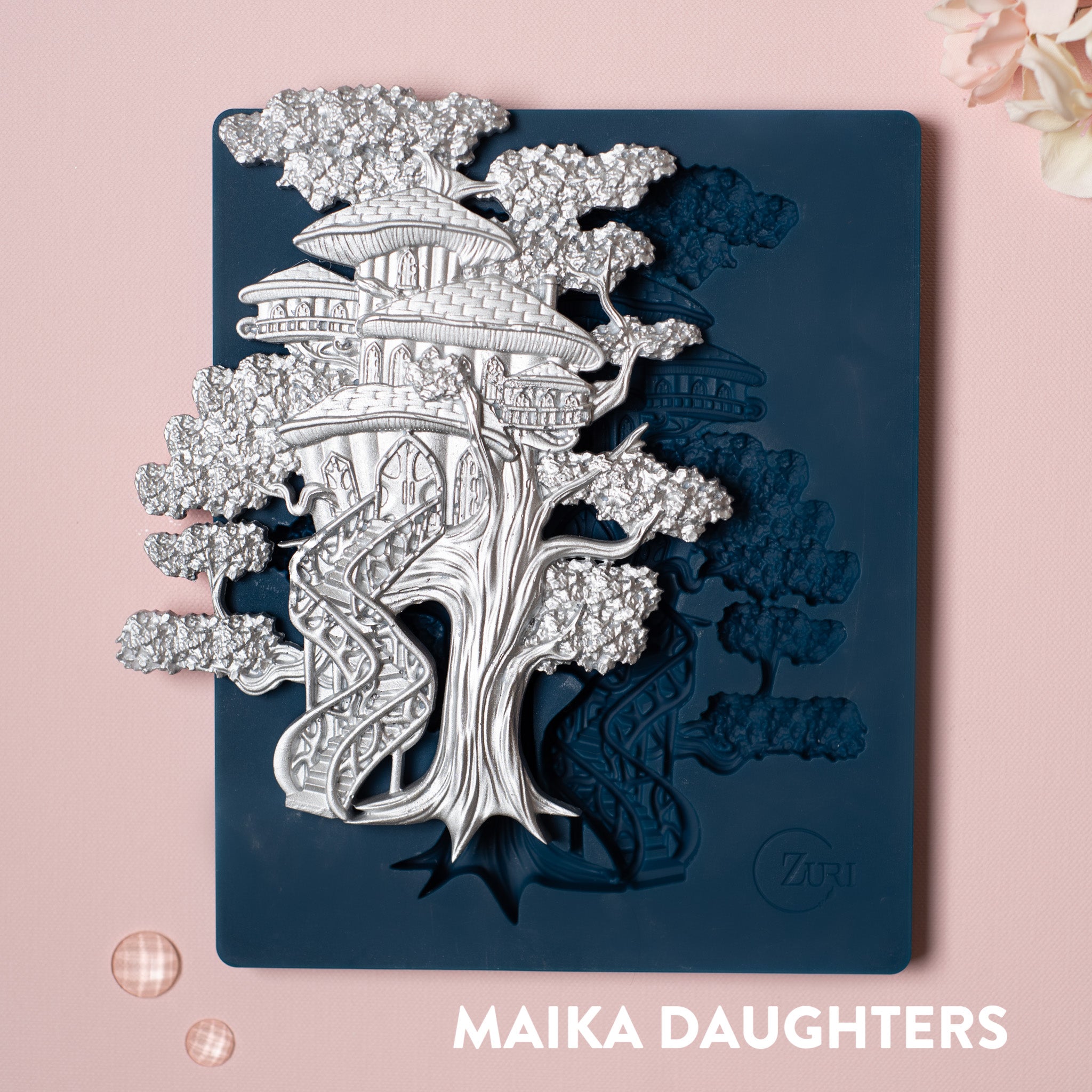 A blue silicone mold and silver colored casting of a tree house  made of mushrooms are against a light pink background.