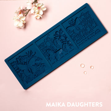 A blue silicone mold of 3 tiles featuring butterflies, flowers and calligraphy is against a light pink background.