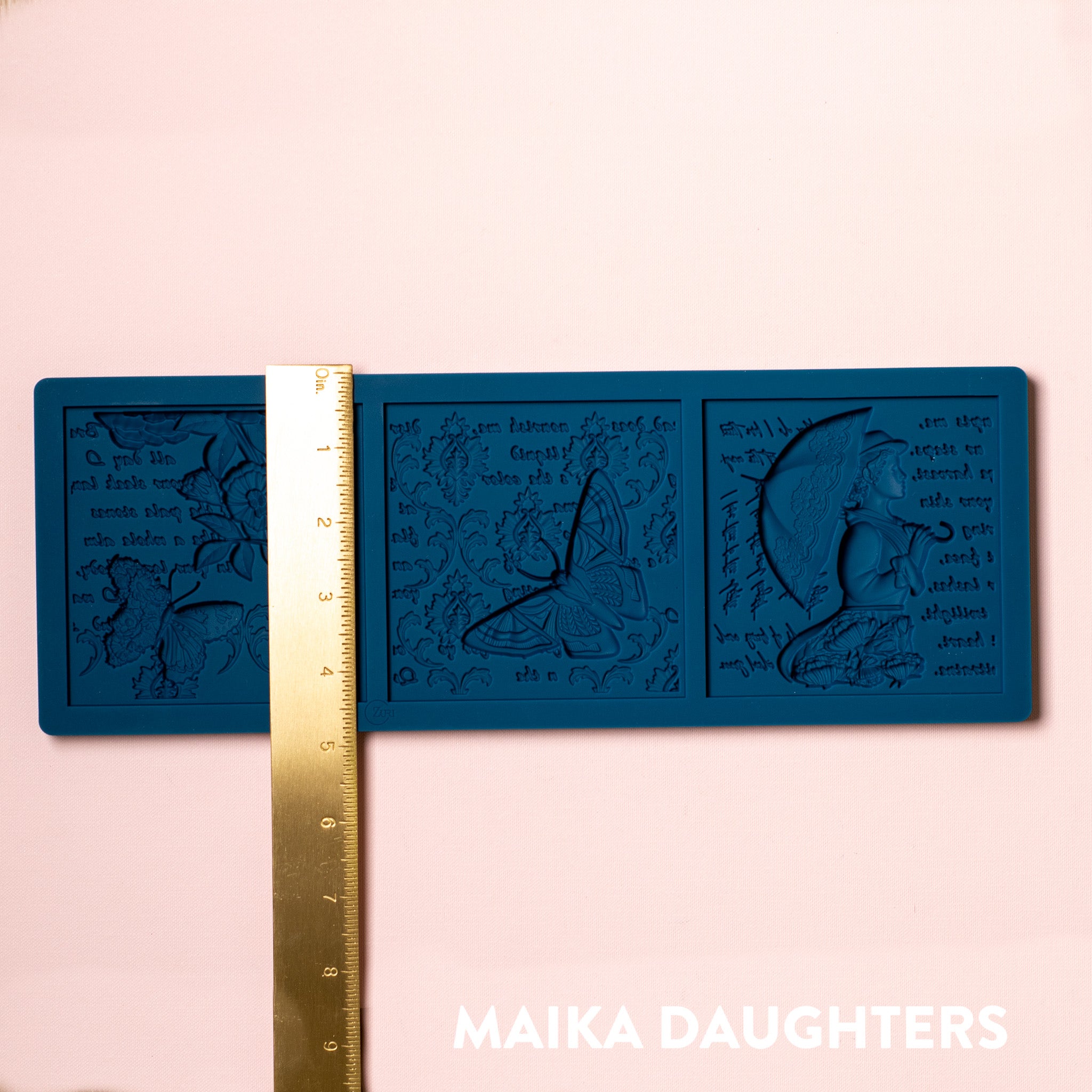 A blue silicone mold of 3 tiles featuring a woman holding an umbrella, butterflies, flowers, and script writing is against a light pink background. A gold ruler reading 4.8" height sits on the mold.