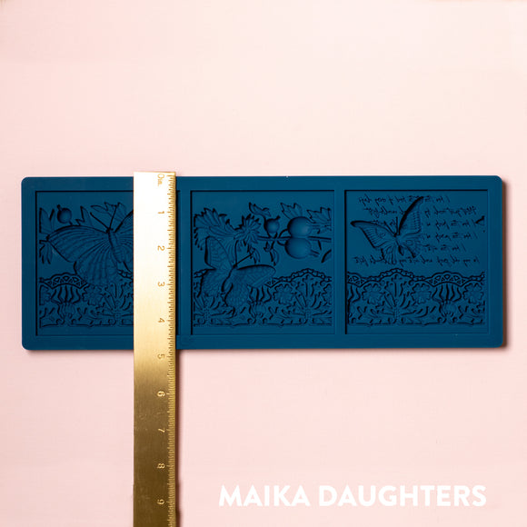 A blue silicone mold of 3 tiles featuring butterflies, a lace border, and script writing is against a light pink background. A gold ruler reading 4.8" height sits on the mold.