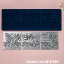 A blue silicone mold and silver colored castings of 3 tiles featuring butterflies, a lace border, and script writing are against a light pink background.