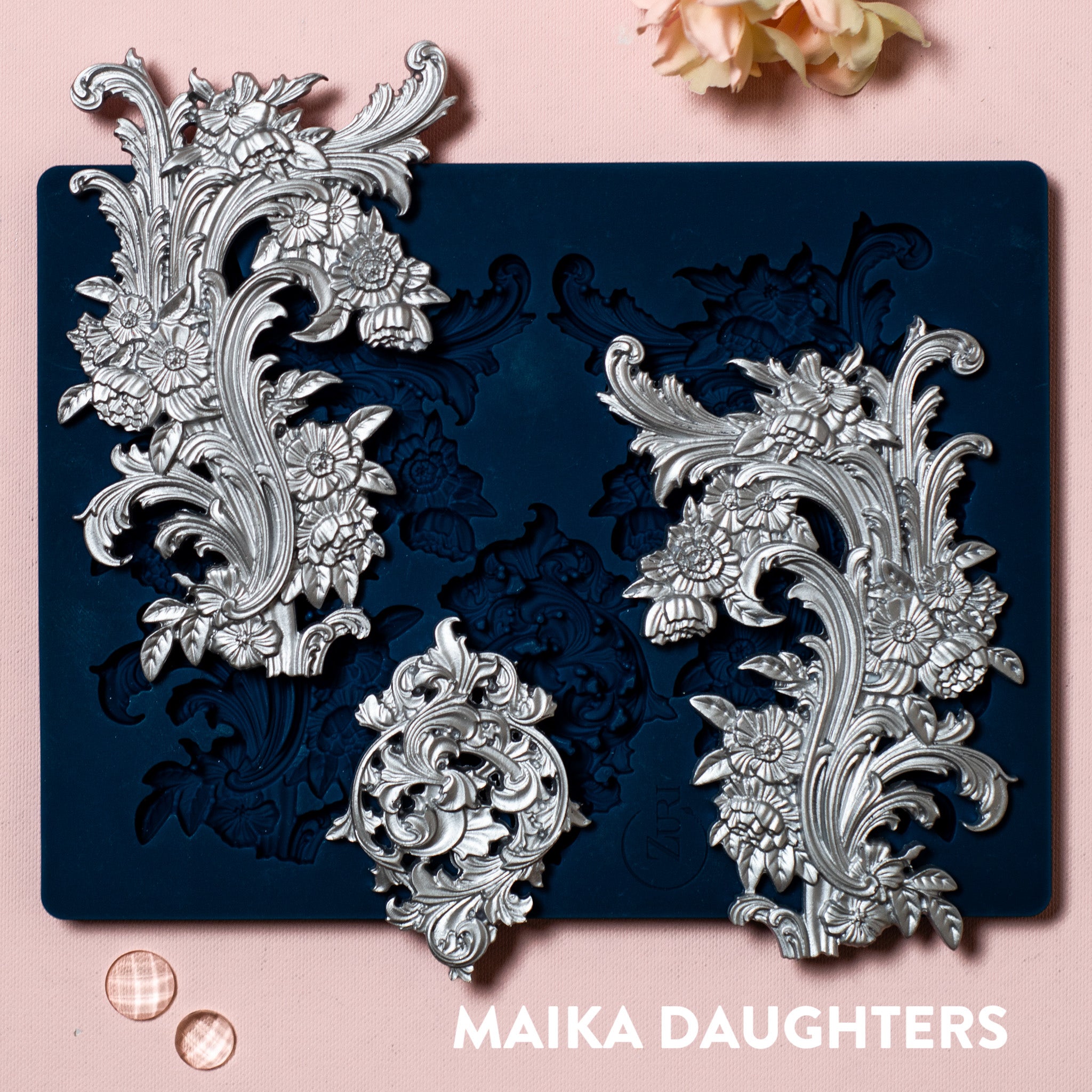 A blue silicone mold and silver colored castings of Zuri Design's Flourishes Set 1 Large are against a light pink background. 