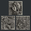 Silver colored castings of 3 tiles featuring a woman holding an umbrella, butterflies, flowers, and script writing are against a dark grey background.