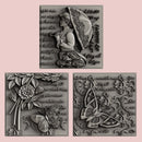 Silver colored castings of 3 tiles featuring a woman holding an umbrella, butterflies, flowers, and script writing are against a light pink background.