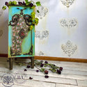 A vintage small side table refurbished by Mustard Tree Market, A Dixie Belle Paint Company Brand Ambassador, is painted a blend of teal and green and features the Peony Pattern A1 rice paper on the front. Dried roses are scattered on and around the table.