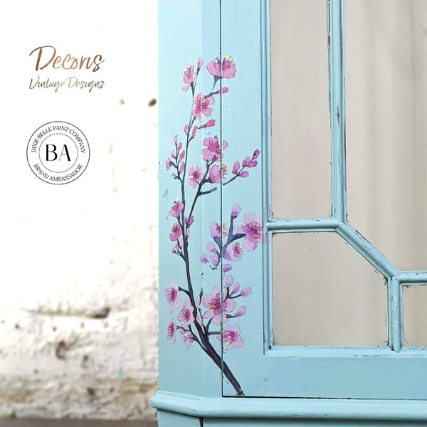 A close-up of a cabinet refurbished by Decoris Vintage Designs, a Dixie Belle Paint Company Brand Ambassador, is painted sky blue and features the Cherry Blossom transfer.