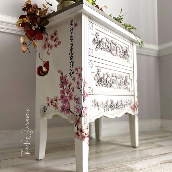 A 2-drawer nightstand refurbished by The Top Drawer is painted white and features the Cherry Blossom transfer on the sides and wraps around to the front.