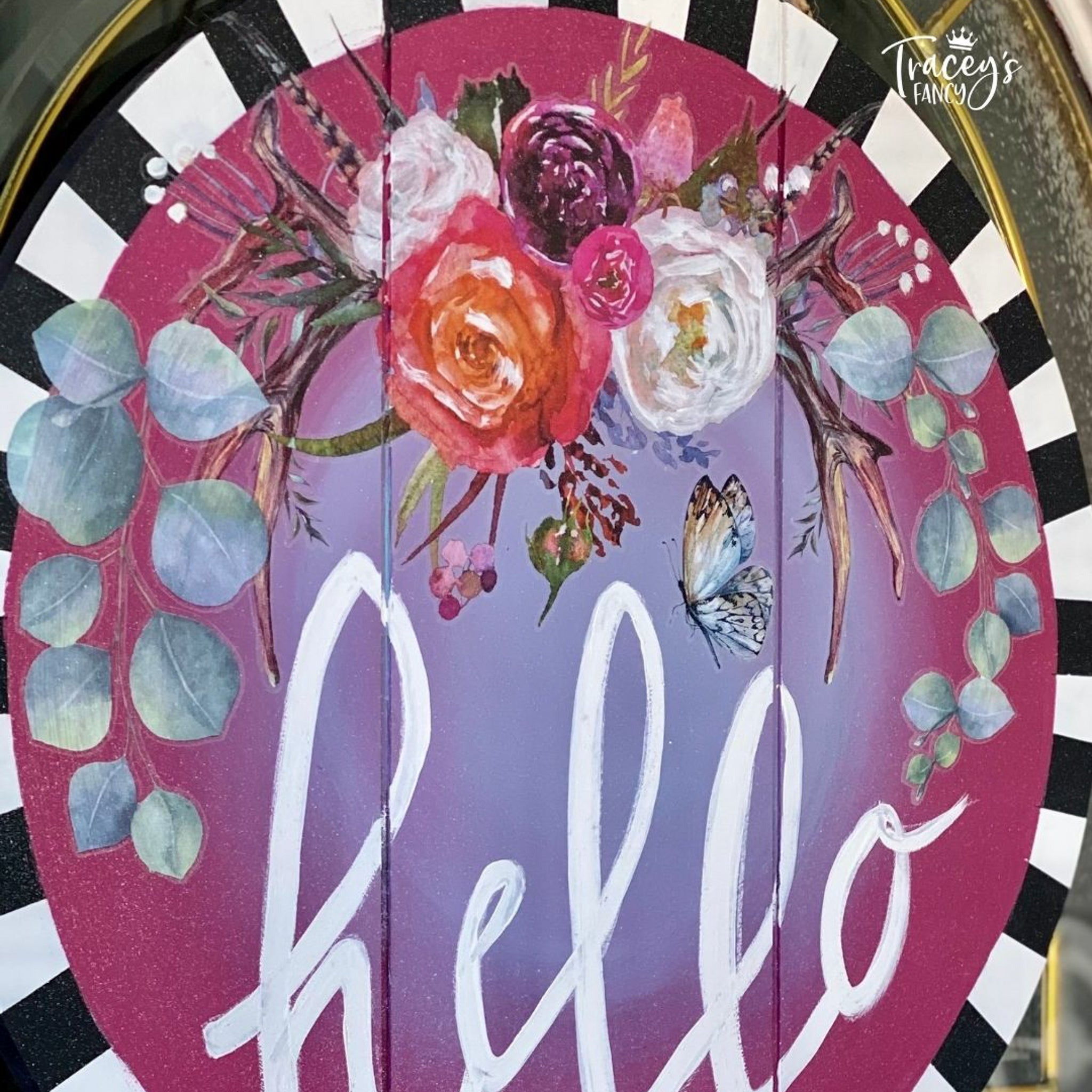 A wood oval craft created by Tracey's Fancy is painted in pink and lavender with Hello painted in white cursive has a black and white checker border and features some of the Flower Child transfer.