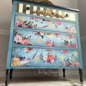 A vintage 4-drawer dresser refurbished by The Top Drawer is painted in sky blue and features the Flower Child transfer on its bottom 3 drawers. The top drawer is painted cream and olive green thick verticle stripes.