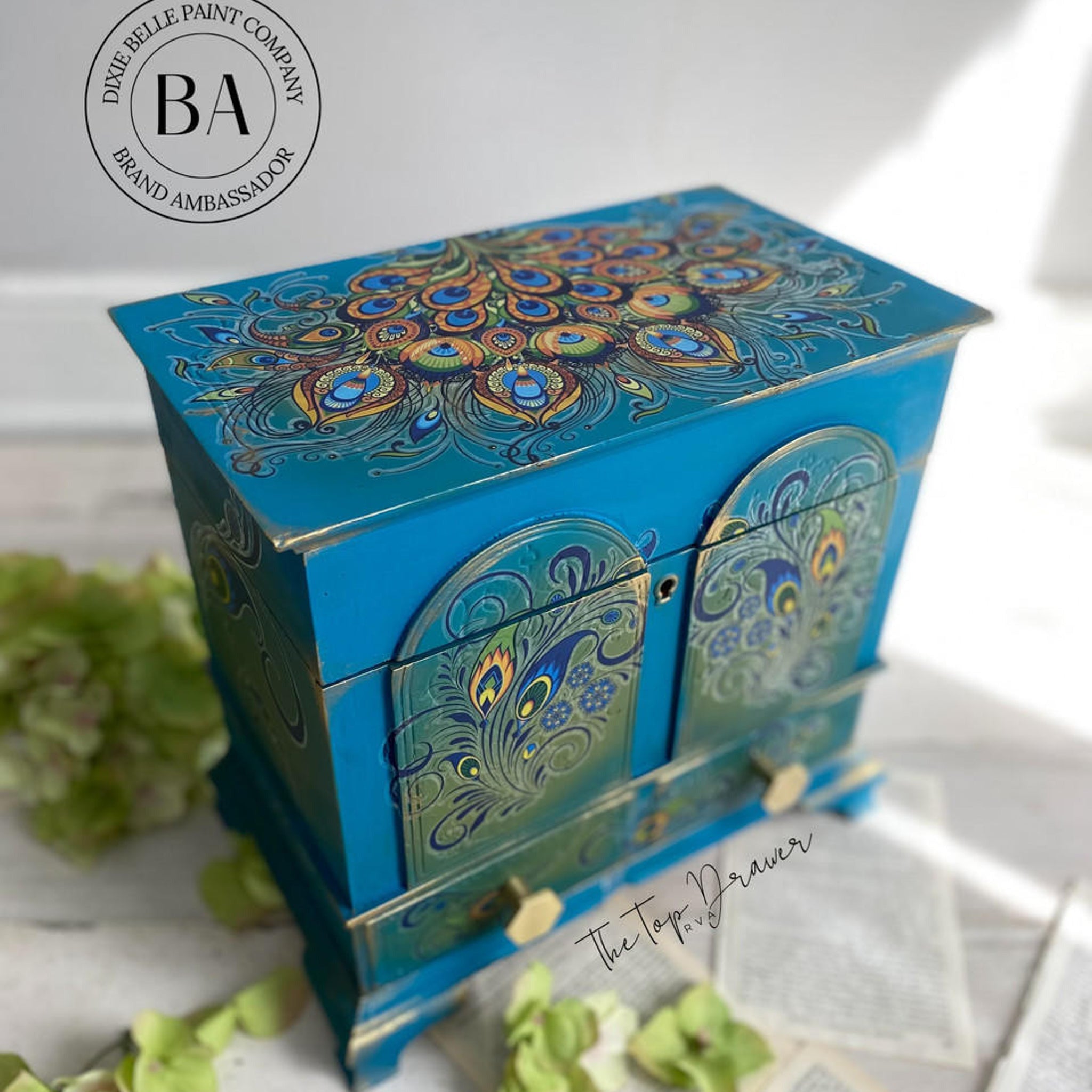 A vintage jewelry box refurbished by The Top Drawer, a Dixie Belle Paint Company Brand Ambassador, is painted a blend of blues and green and features the Retro Peacock transfer.