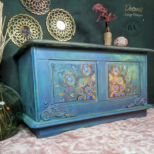 A vintage wood storage chest refurbished by Decoris Vintage Designs, a Dixie Belle Paint Company Brand Ambassador, is painted a distressed blue and green and features the Retro Peacock transfer on the front of it.