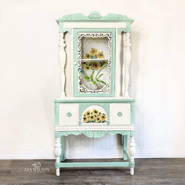 A vintage small hutch refurbished by Lyn Wilson Originals is painted white and mint green and features the Sunflowers Transfer on the front center and inside the backboard of the hutch cabinet.