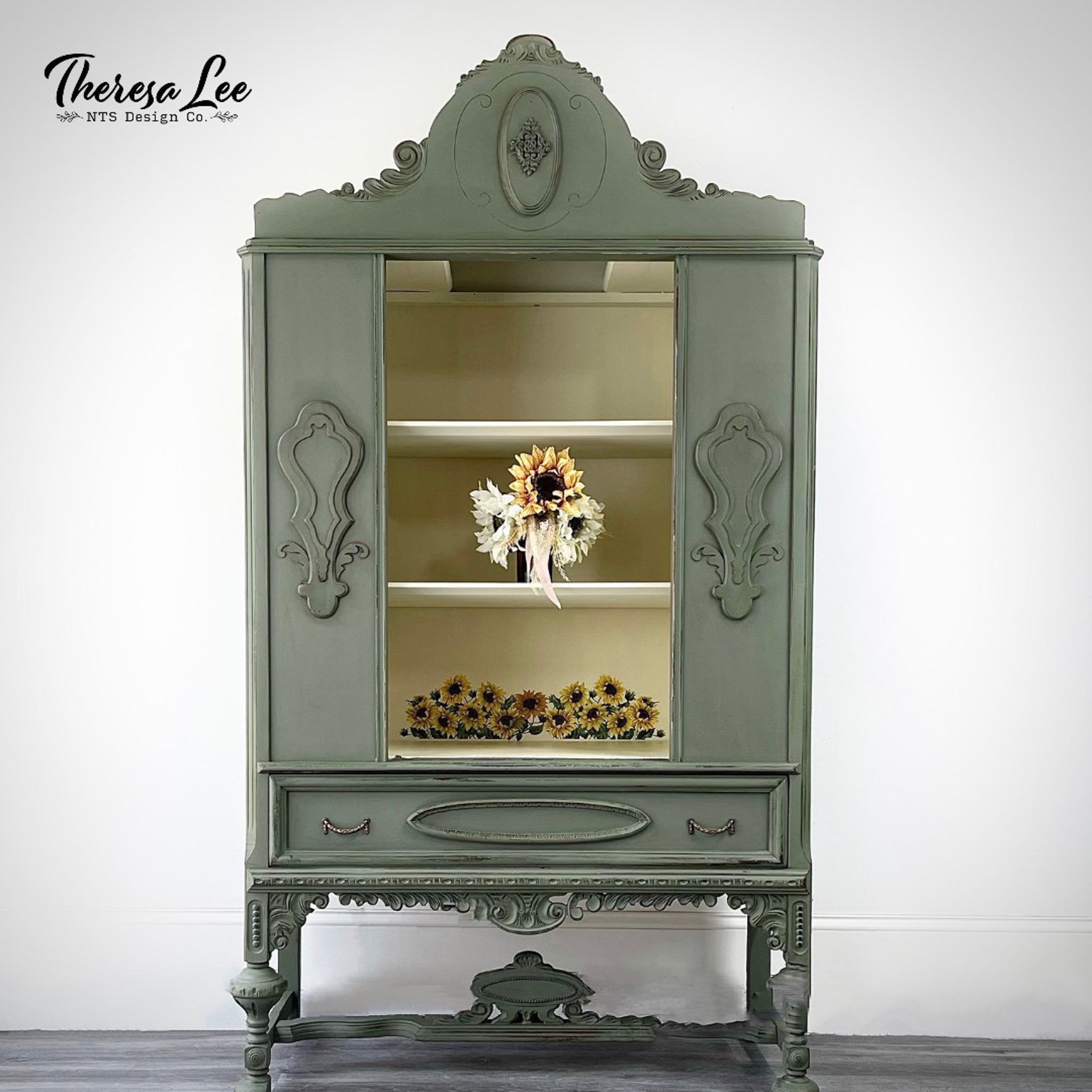 A vintage armoir refurbished by Theresa Lee NTS Design Company is painted sage green. Inside is painted cream and features the Sunflower Transfer on its backboard at the bottom.
