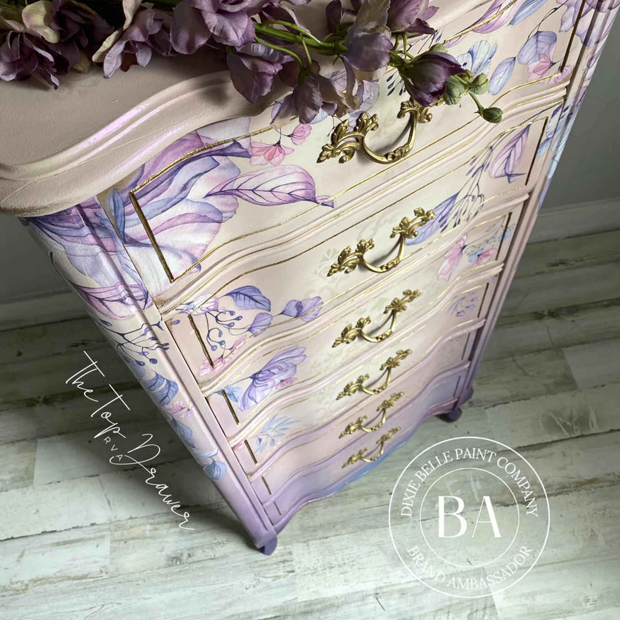 An aerial view of a tall French Provencial chest dresser refurbished by The Top Drawer, a Dixie Belle Paint Company Brand Ambassador, is painted light beige and light purple and features the Translucent Garden Transfer on it.