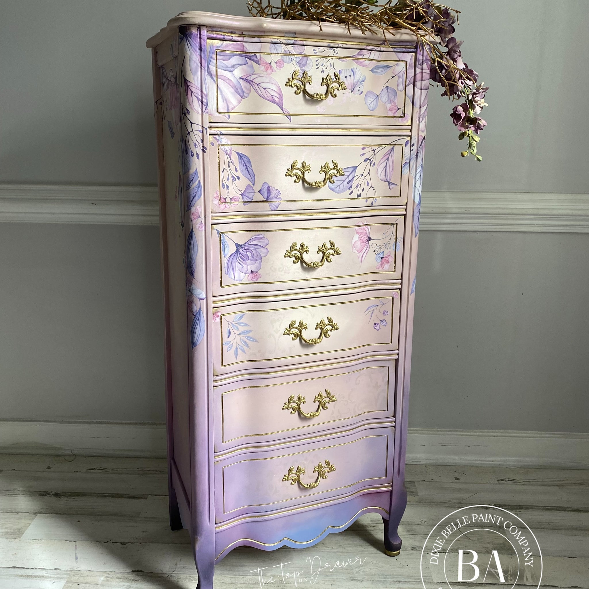A tall French Provencial chest dresser refurbished by The Top Drawer, a Dixie Belle Paint Company Brand Ambassador, is painted light beige and light purple and features the Translucent Garden Transfer on it.