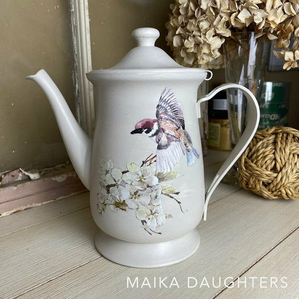 A white tea pot with the Blossom Flight transfer on top. A white Maika Daughters logo on the bottom right.