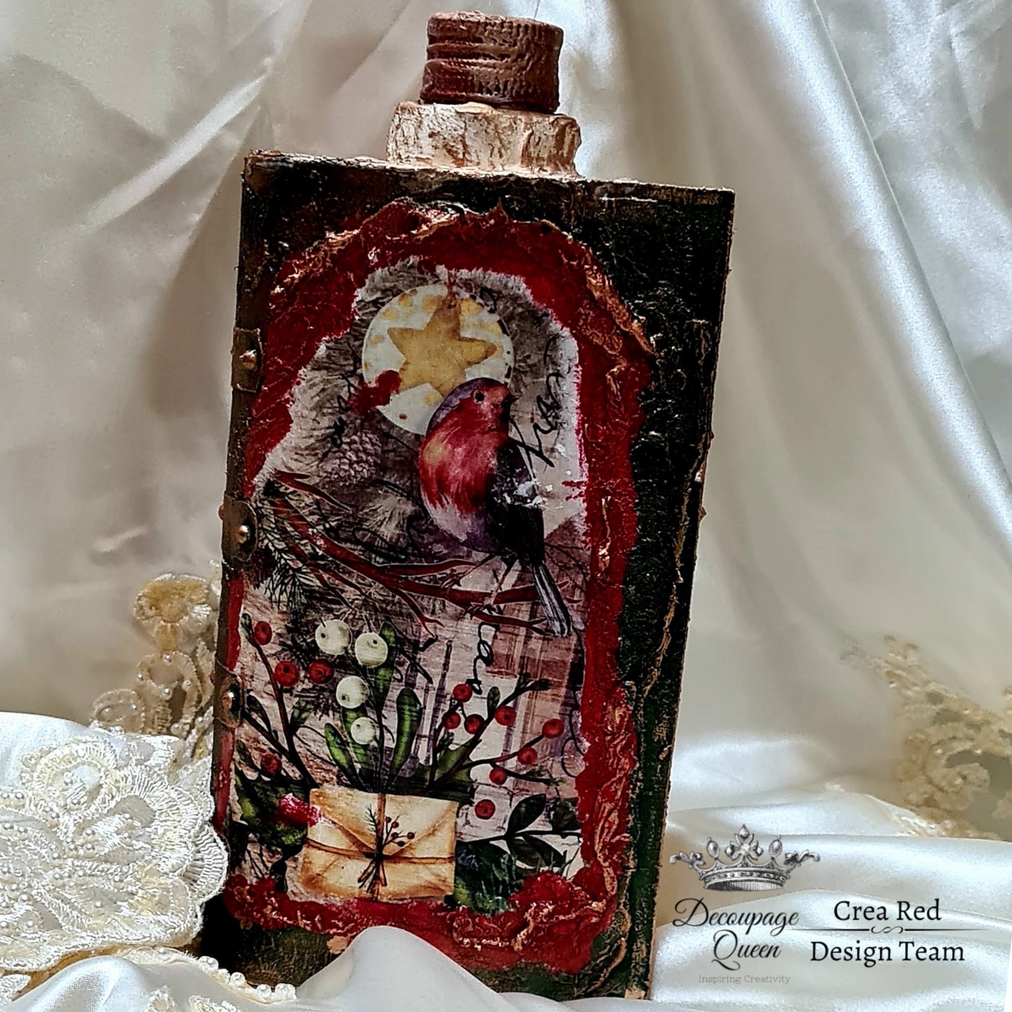 A decor flask with the Festive Robins decoupage paper on top. A black Decoupage Queen and Crea Red Design Team logo on the bottom right.