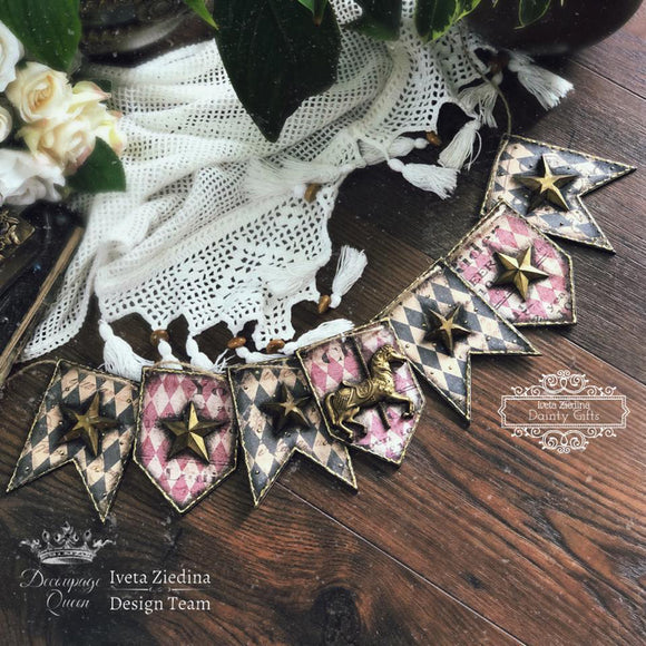 A bunting banner laying on a dark wood floor with gold colored silicone mold castings of stars and a carousel horse features Decoupage Queen's Sheila's Black Harlequin rice paper on them.