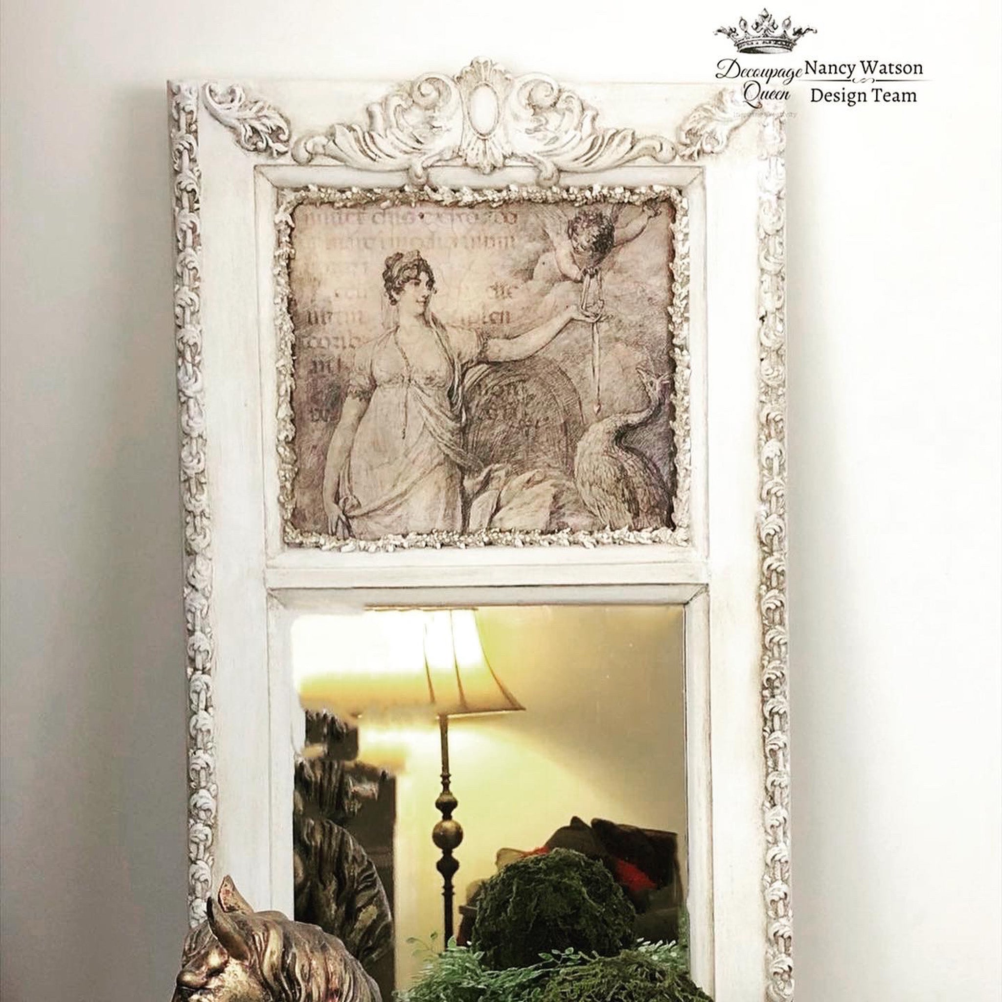 White ornate mirror with the Juno and Cupid decoupage paper on top. A black Decoupage Queen and Nancy Watson Design Team logo on the top right.