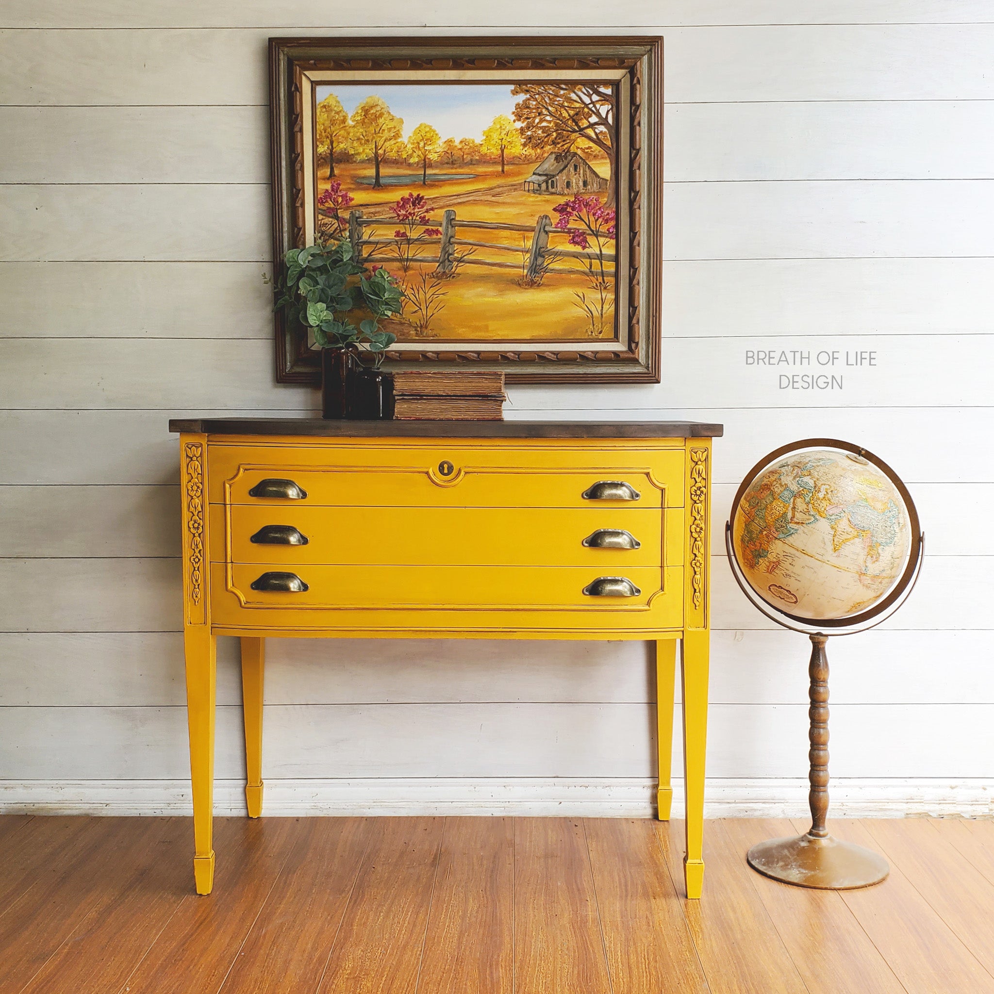 A vintage 3-drawer console table refurbished by Breath of Life Design is painted in Dixie Belle's Colonel Mustard chalk mineral paint and has a natural dark wood top on it.