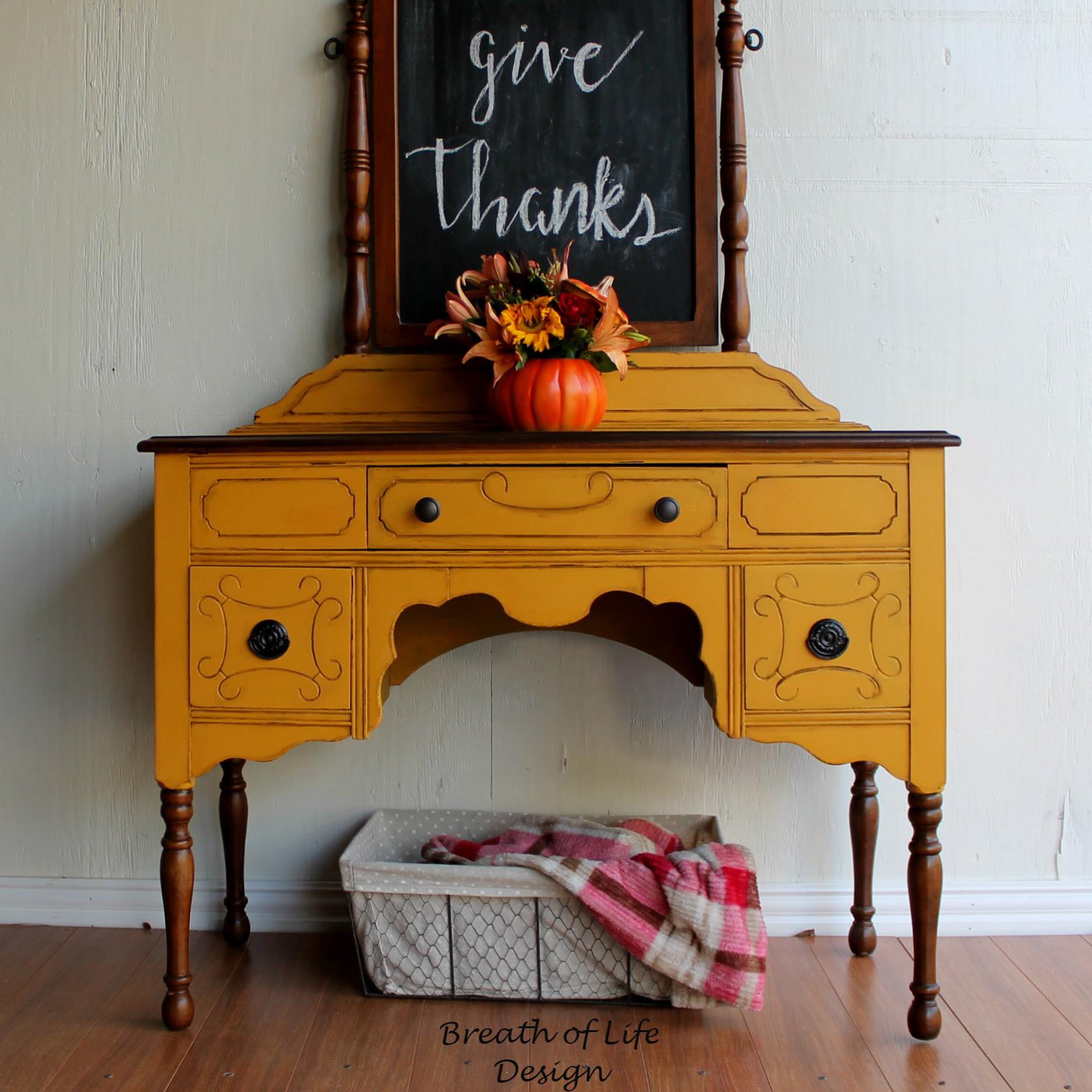 A vintage console table refurbished by Breath of Life Design is painted in Dixie Belle's Colonel Mustard chalk mineral paint with natural dark wood accents.