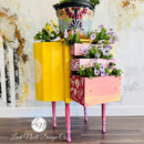 A vintage 3-drawer nightstand turned into a planter refurbished by Leah Noell Design Company is painted in Dixie Belle's Daisy chalk mineral paint. The drawers are an ombre of light pink down to coral pink with a painted cactus design.
