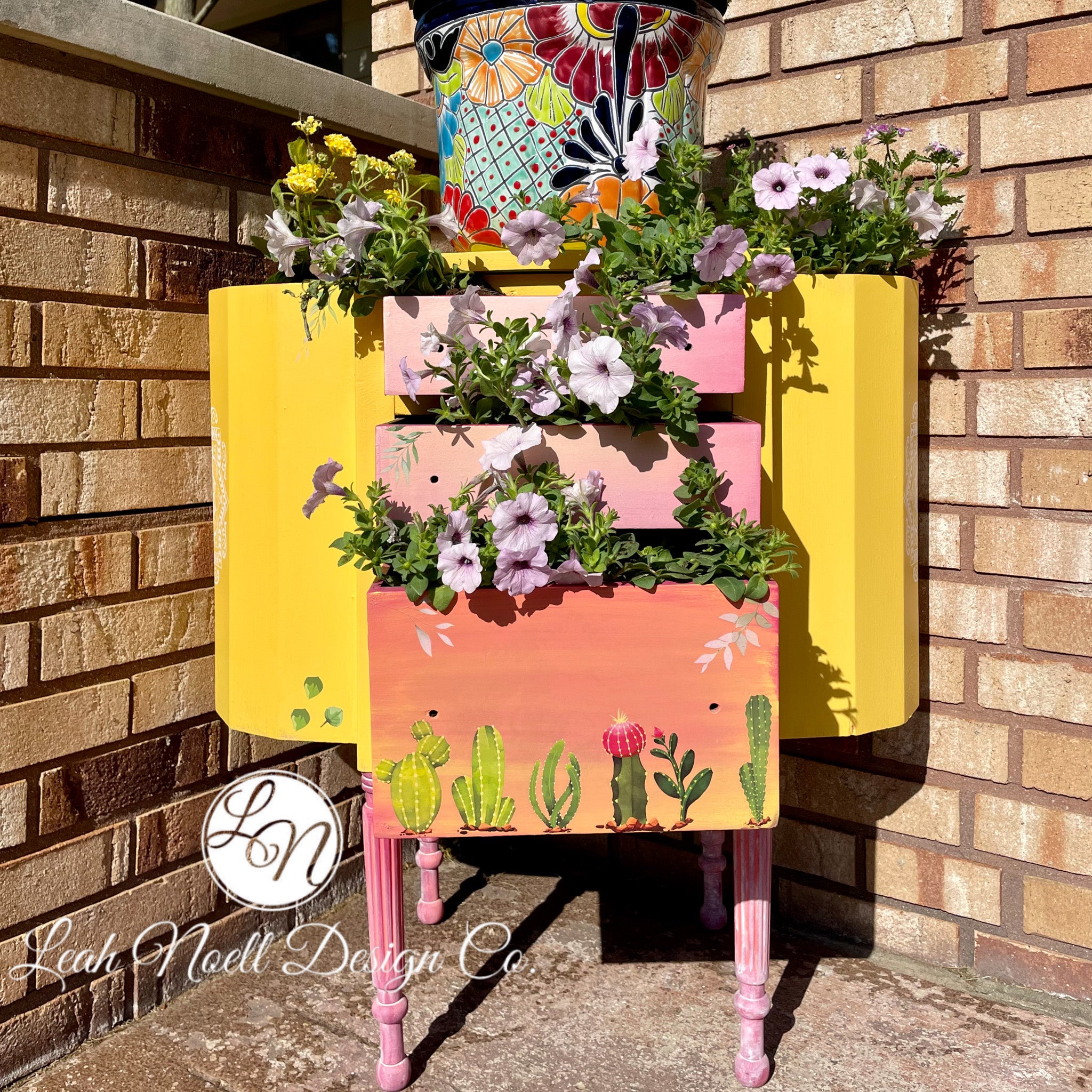 A vintage 3-drawer nightstand turned into a planter refurbished by Leah Noell Design Company is painted in Dixie Belle's Daisy chalk mineral paint. The drawers are an ombre of light pink down to coral pink with a painted cactus design.