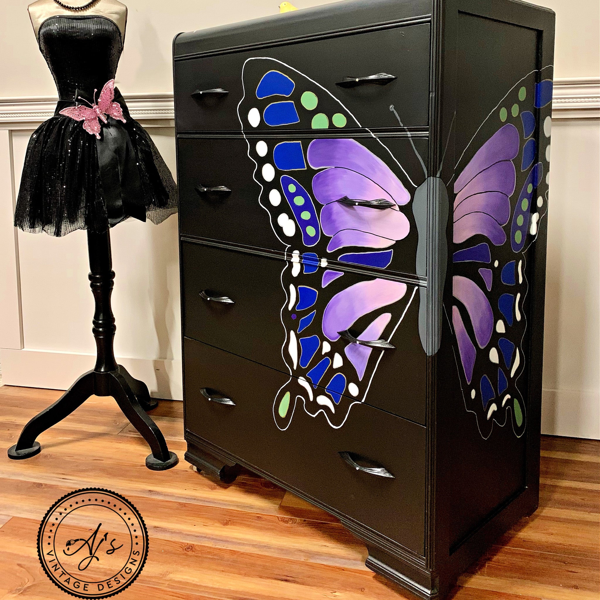 A vintage waterfall dresser refurbished by Aj's Vintage Designs is painted black and has a large butterfly hand-painted on the front right corner wrapping around to the side that features Dixie Belle's Lucky Lavender chalk mineral paint.