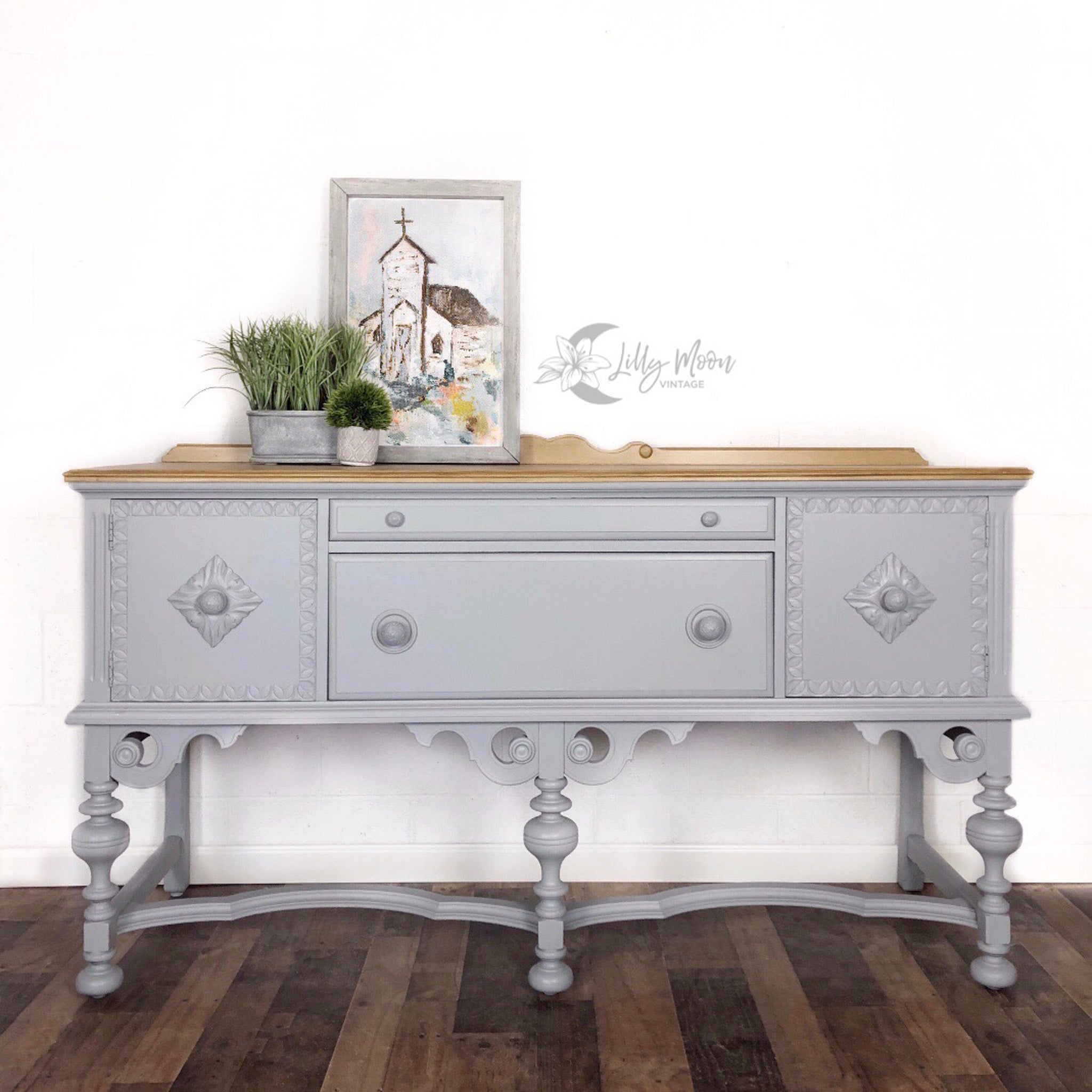 A vintage console table with storage refurbished by Lilly Moon Vintage is painted in Dixie Belle's Manatee Gray chalk mineral paint and has a natural wood top on it.
