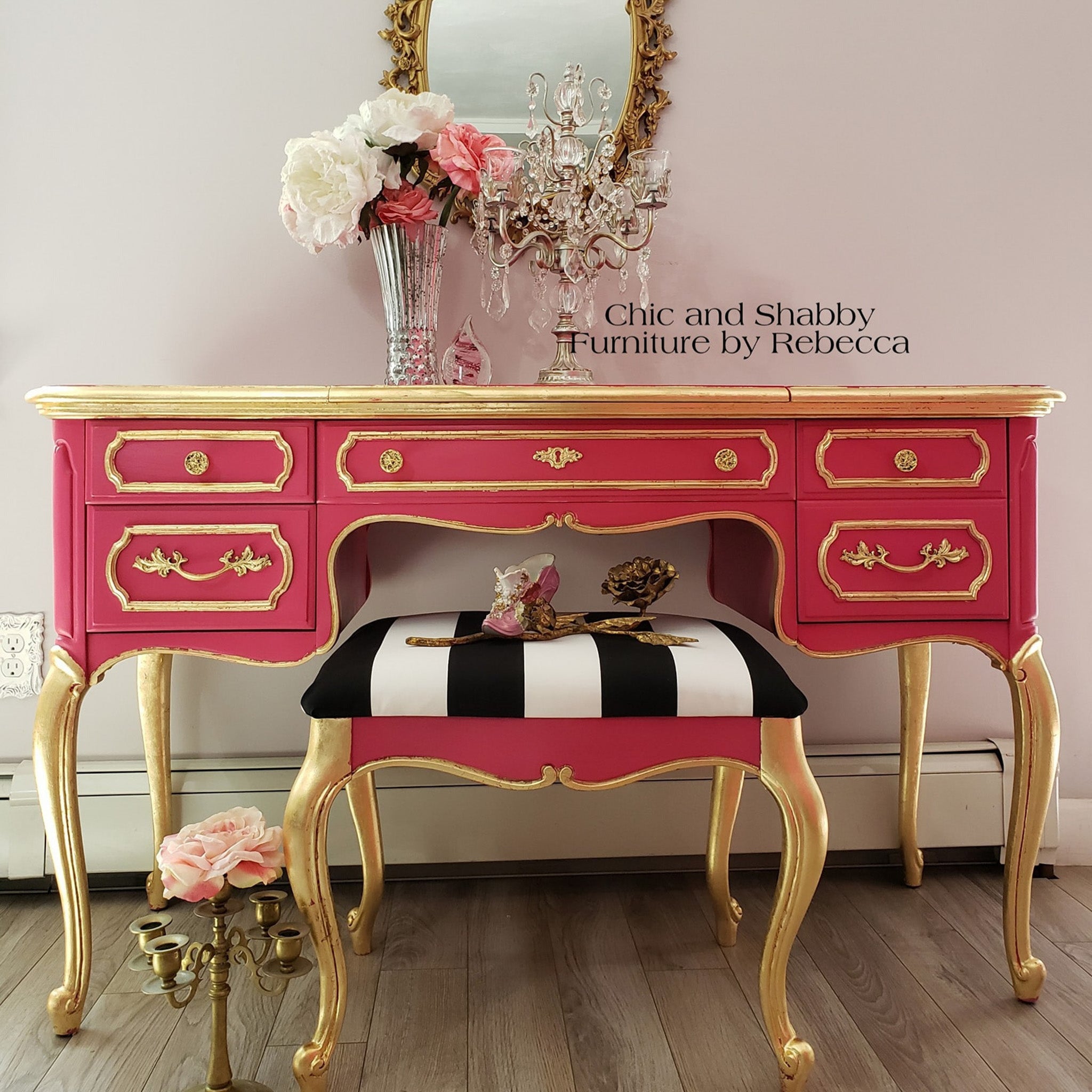 A vintage vanity and stool refurbished by Chic and Shabby Furniture by Rebecca is painted in Dixie Belle's Peony chalk mineral paint and is accented with gold trim and legs.