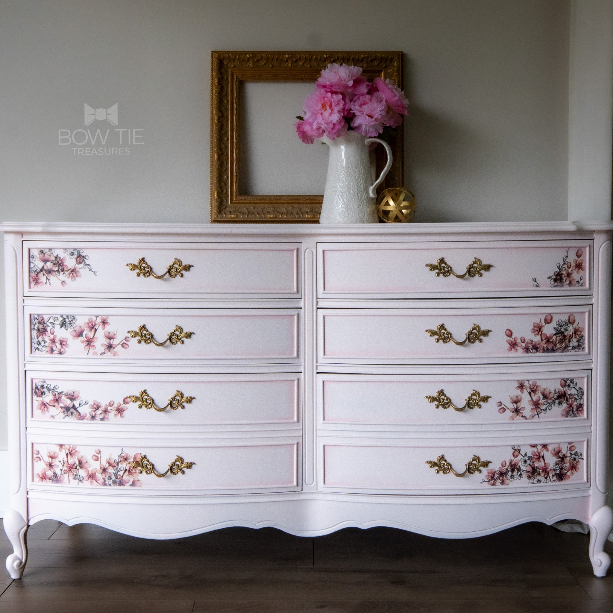 A vintage 8-drawer dresser refurbished by Bow Tie Treasures is painted in Dixie Belle's Soft Pink chalk mineral paint and has pink flower transfers on the drawers.