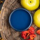 An arial view of an open container of Dixie Belle Paint Company's Bunker Hill Blue Chalk Mineral Paint is in a wicker basket surrounded by fruit and flowers.