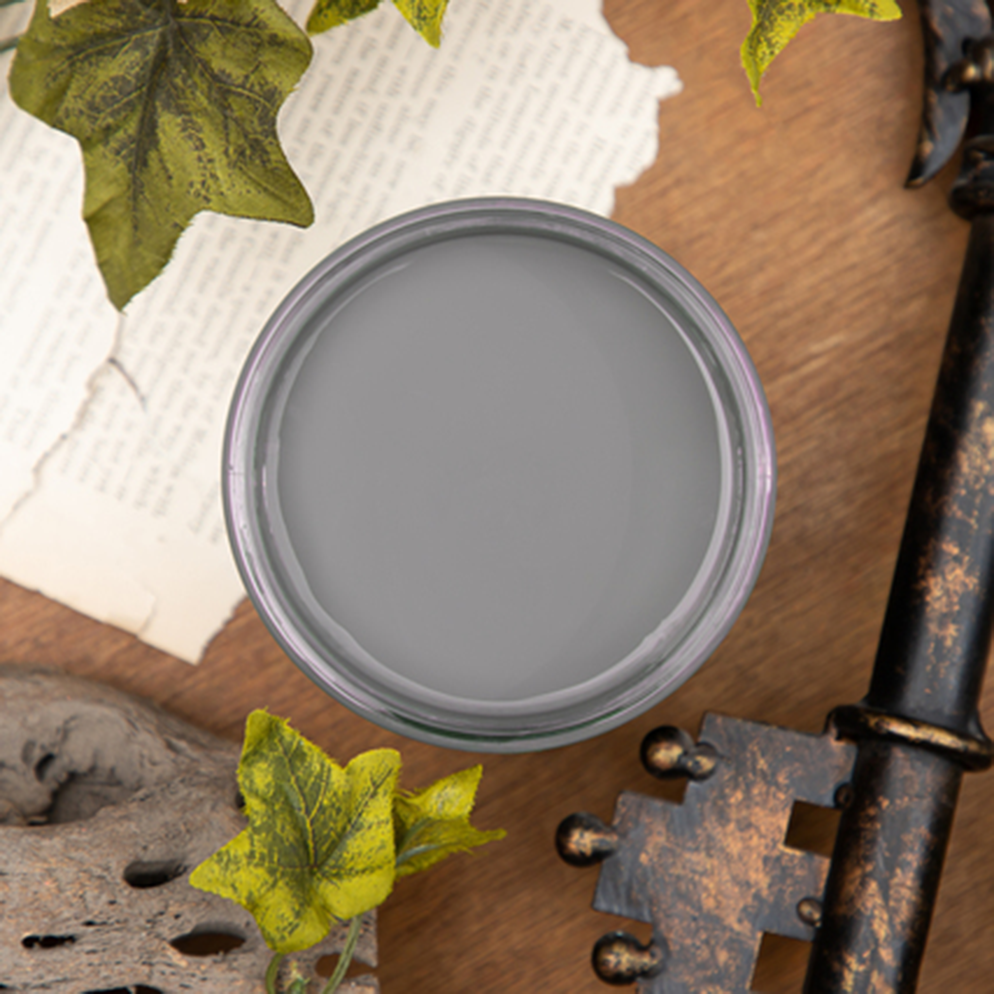 An arial view of an open container of Dixie Belle Paint Company’s Hurricane Gray Chalk Mineral Paint is against a wood background with leaves, a vintage key, and a torn piece of parchment.