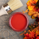 An arial view of an open container of Dixie Belle Paint Company's Barn Red Chalk Mineral Paint is surrounded by flowers and a paint brush.
