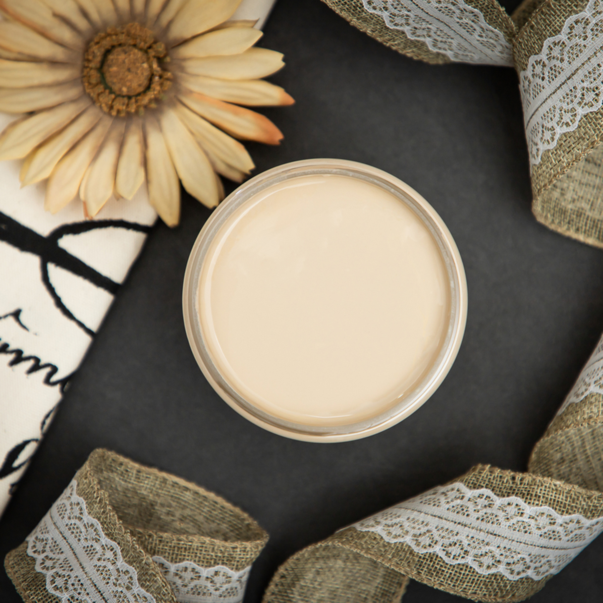 An arial view of an open container of Dixie Belle Paint Company's Burlap Chalk Mineral Paint is surrounded by burlap with lace ribbon and a dried daisy flower.