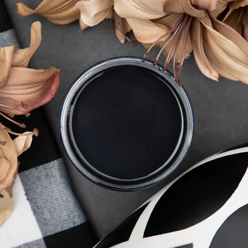 An arial view of an open container of Dixie Belle Paint Company's Caviar Chalk Mineral Paint is surrounded by tan silk flowers.