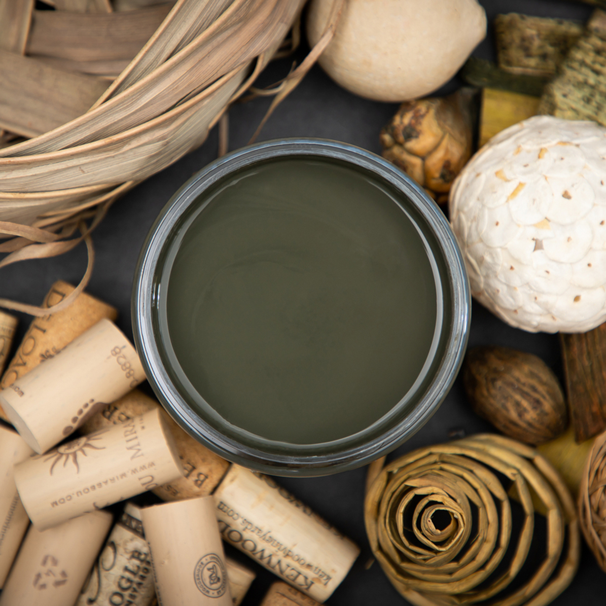 An arial view of an open container of Dixie Belle Paint Company’s Collard Greens Chalk Mineral Paint is surrounded by bottle corks, nuts, and a brown wicker basket.