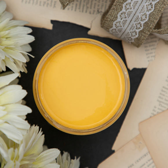 An arial view of an open container of Dixie Belle Paint Company’s Daisy Chalk Mineral Paint is surrounded by burlap lace ribbon, Gerber daisies, and old book pages.