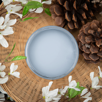 An arial view of an open container of Dixie Belle Paint Company’s Dusty Blue Chalk Mineral Paint is in a wicker basket with white silk flowers and pine cones.