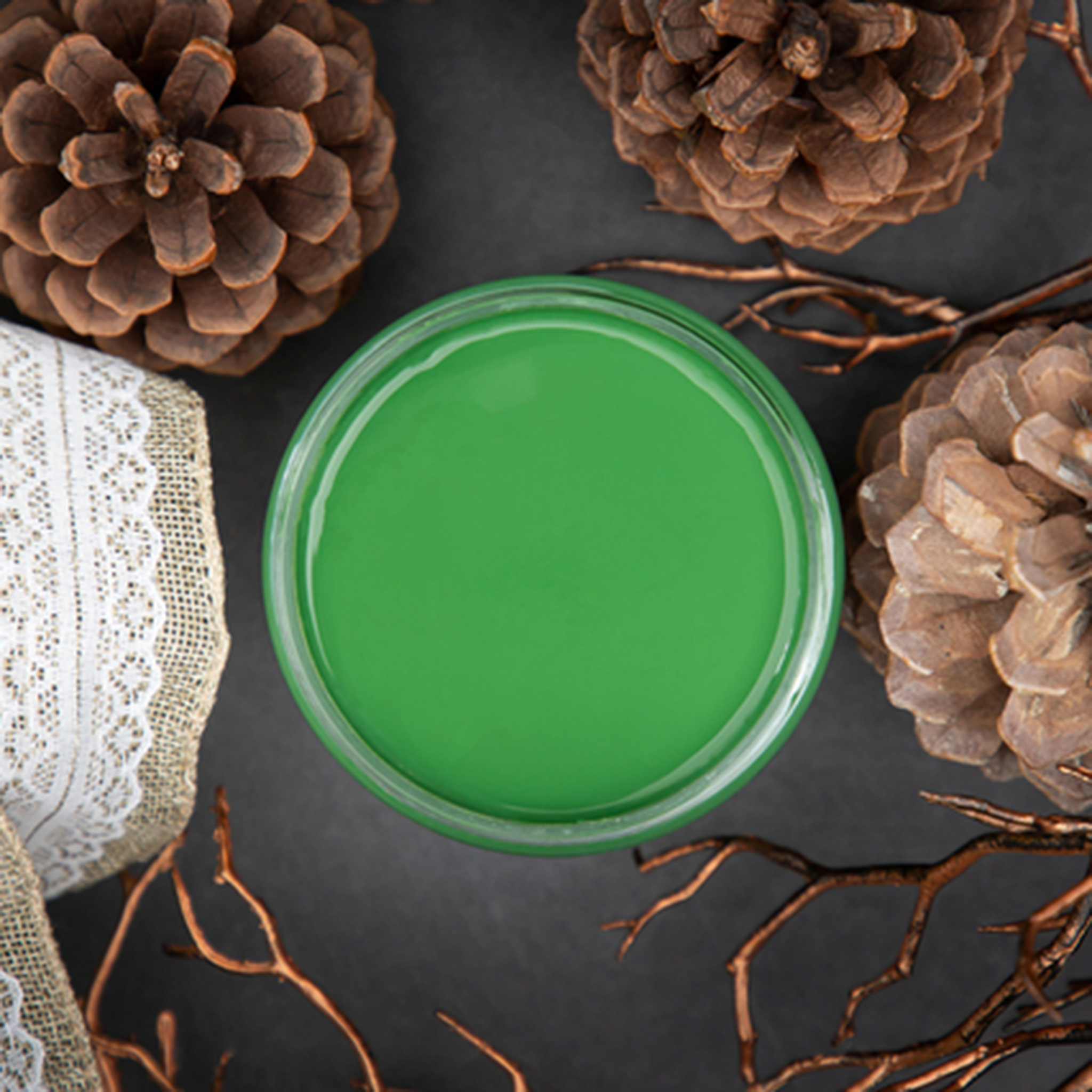 An arial view of an open container of Dixie Belle Paint Company’s Evergreen Chalk Mineral Paint is surrounded by pine cones and burlap lace ribbon.