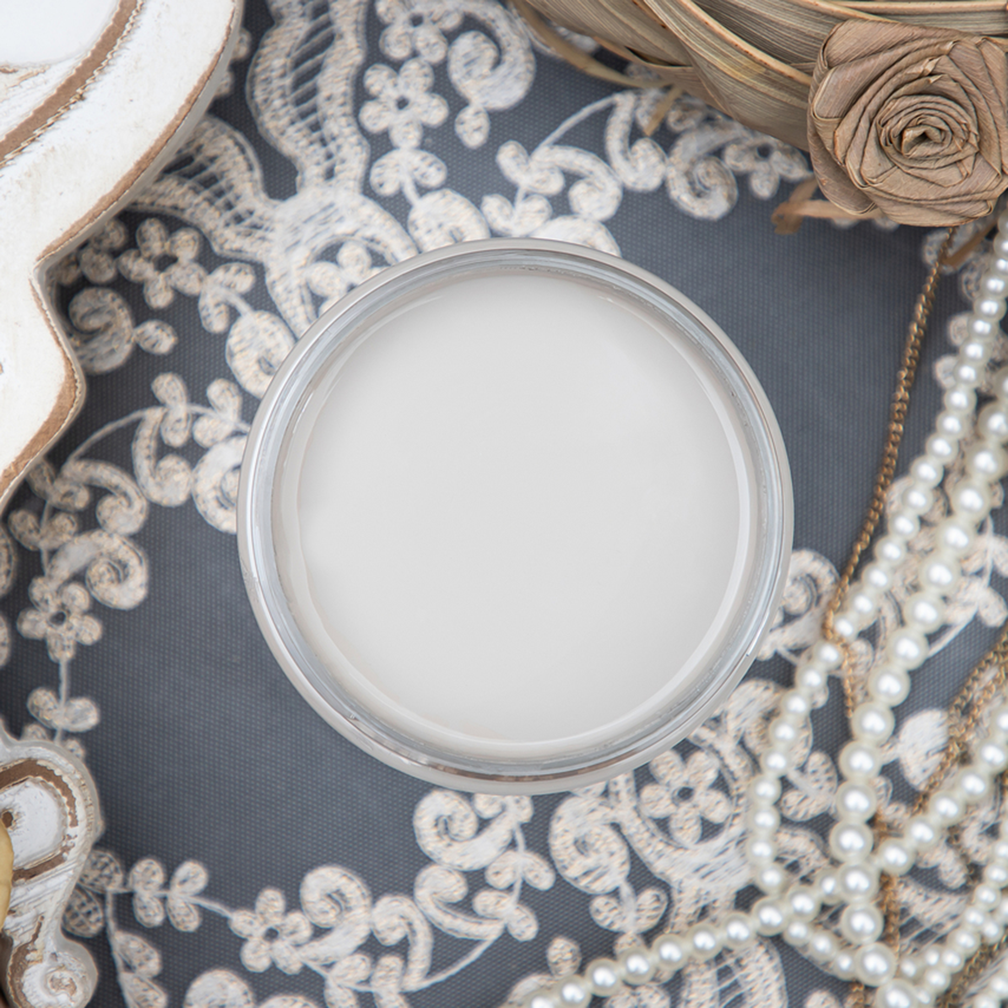 An arial view of an open container of Dixie Belle Paint Company’s French Linen Chalk Mineral Paint sits on a lace background with a pearl necklace.