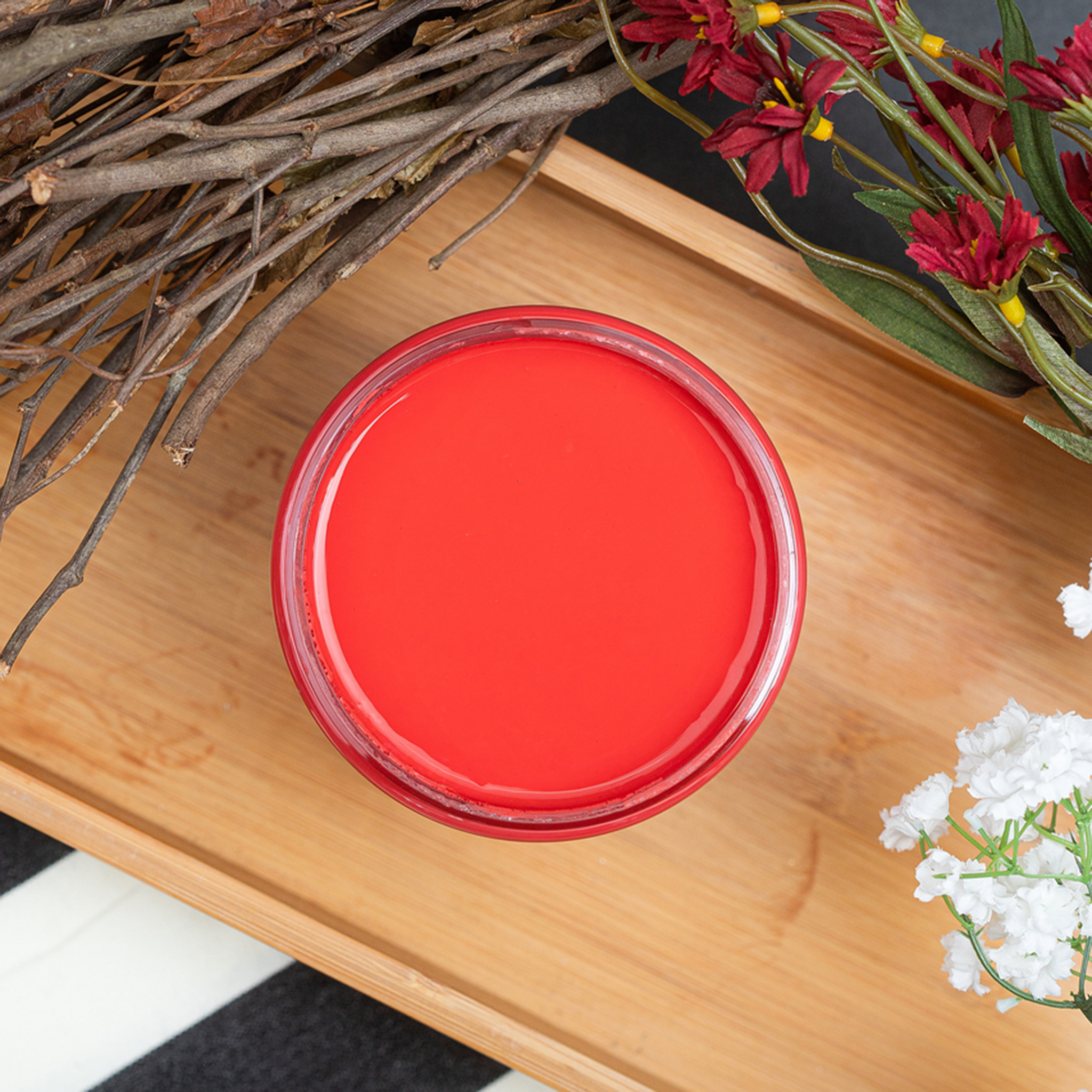 An arial view of an open container of Dixie Belle Paint Company’s Honky Tonk Red Chalk Mineral Paint sits on a wood tray surrounded by branches and red and white silk flowers.