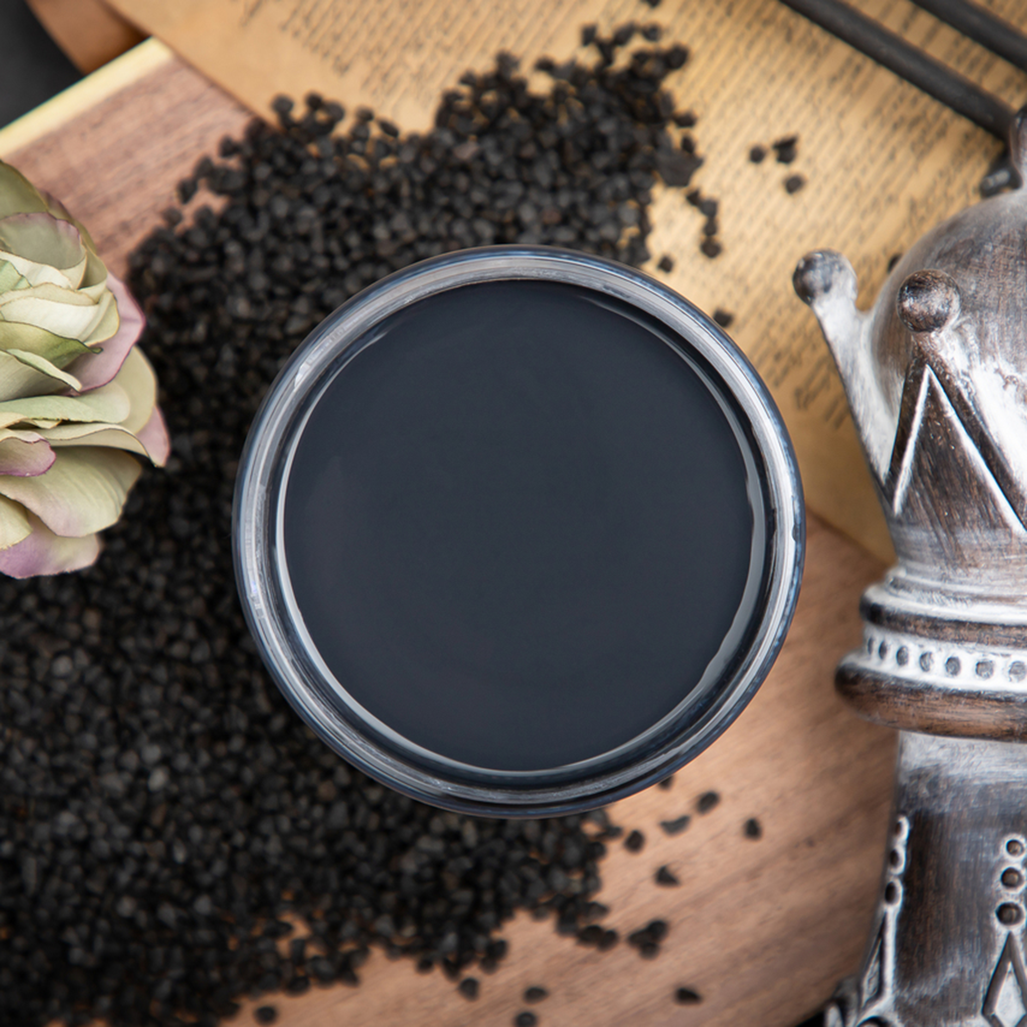 An arial view of an open container of Dixie Belle Paint Company’s Midnight Sky Chalk Mineral Paint is surrounded by small black rocks against a wood table.