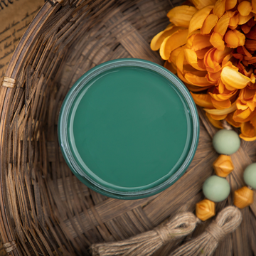 An arial view of an open container of Dixie Belle Paint Company’s Palmetto Chalk Mineral Paint is in a wicker basket with a large orange silk flower with wood beads and twine tassels.