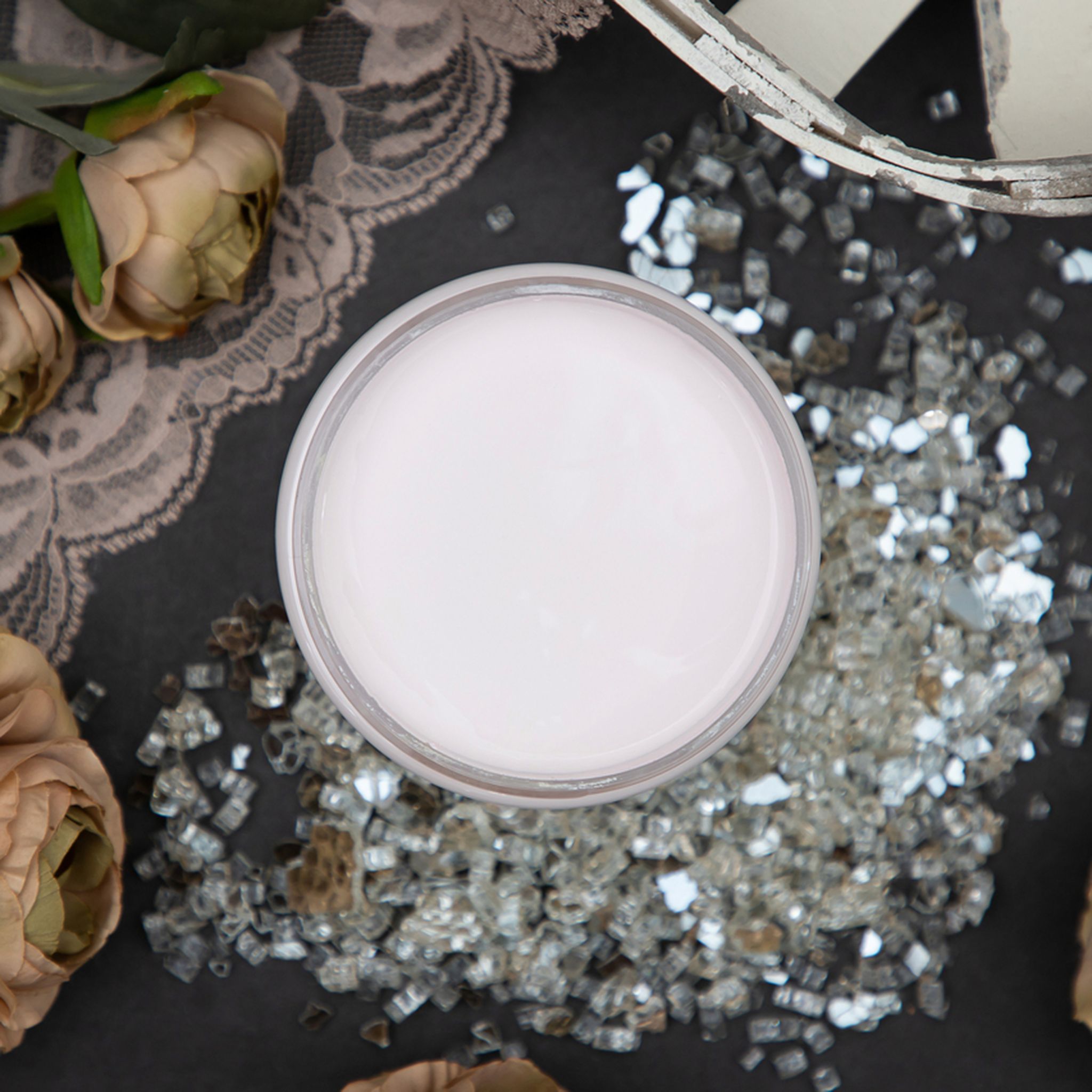 An arial view of an open container of Dixie Belle Paint Company’s Pink Champagne Chalk Mineral Paint is surrounded by roses and glass shards.