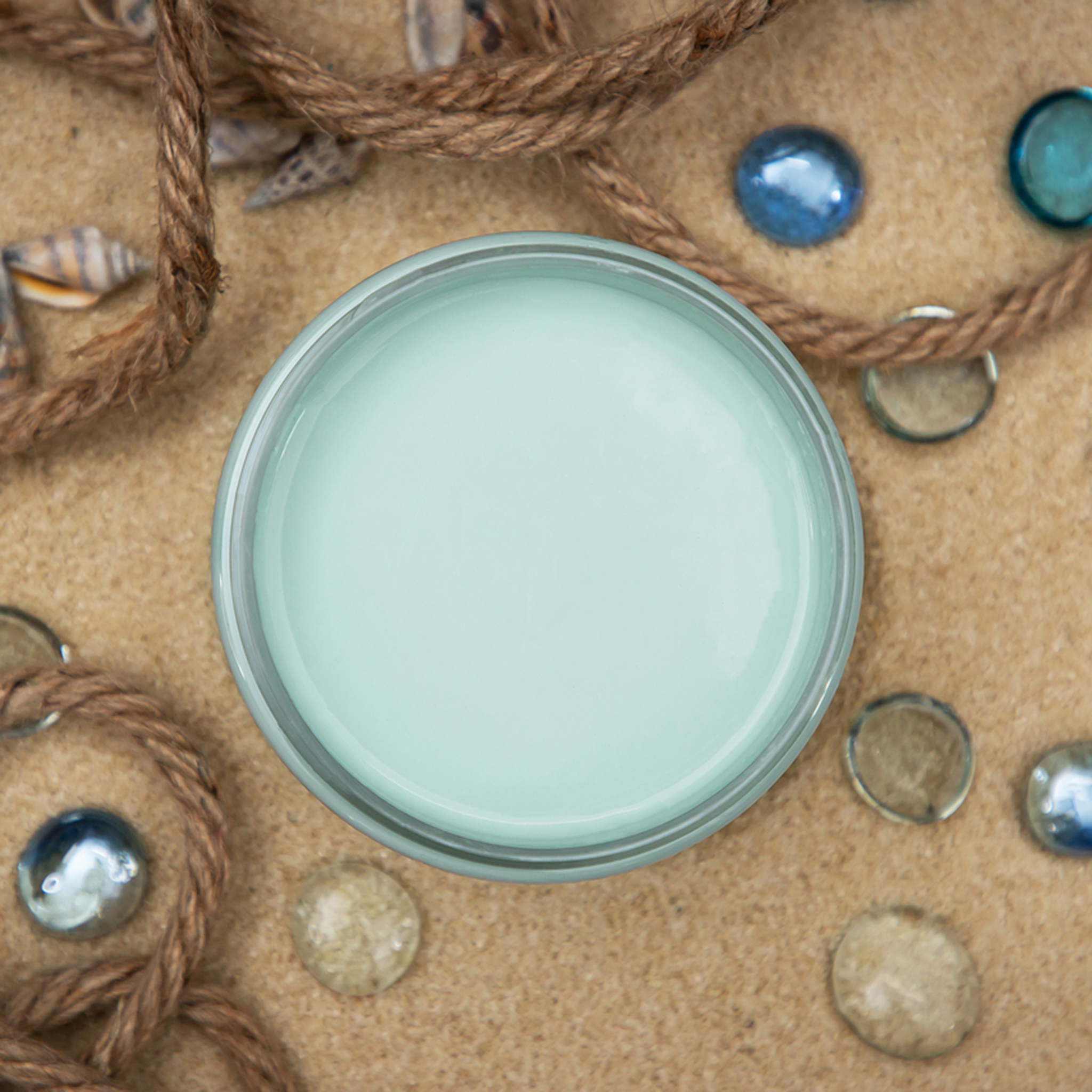 An arial view of an open container of Dixie Belle Paint Company’s Sea Glass Chalk Mineral Paint is surrounded by rope and blue glass decorative marbles.