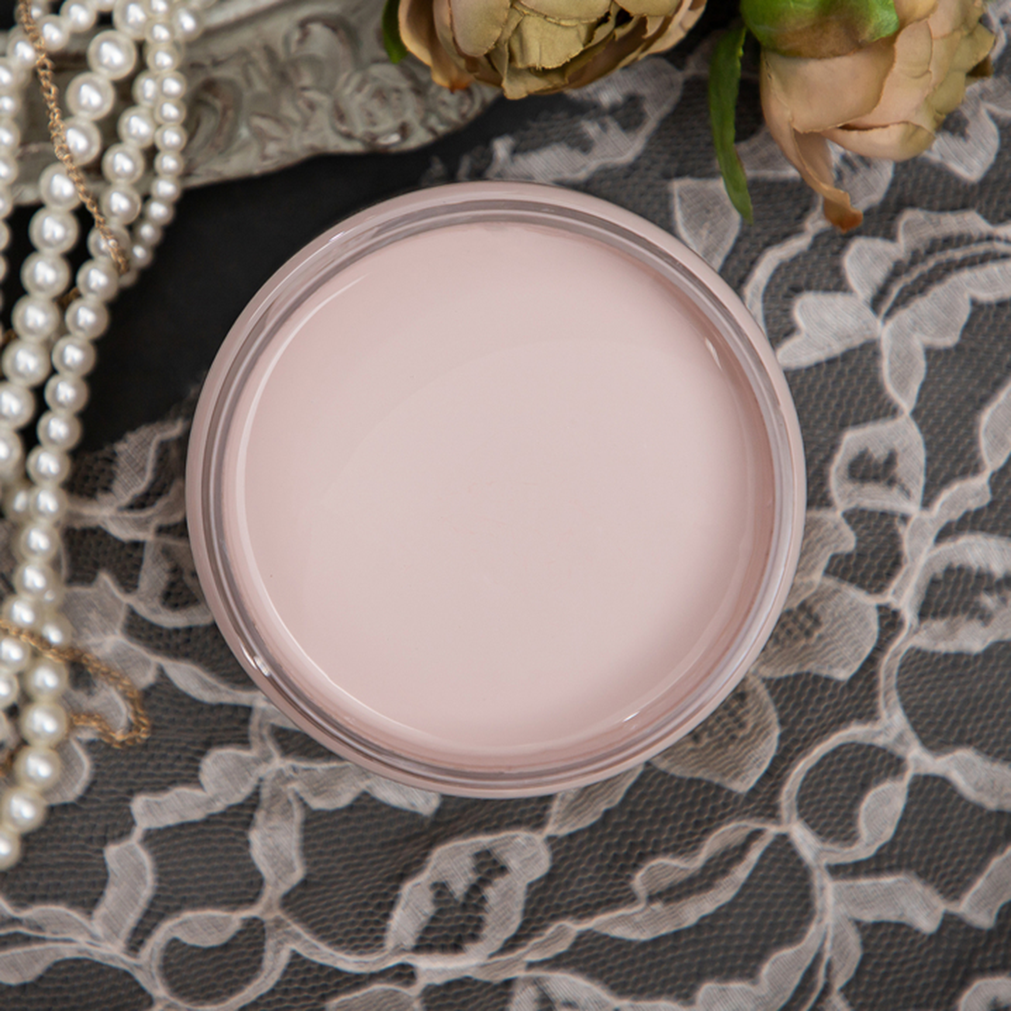 An arial view of an open container of Dixie Belle Paint Company’s Tea Rose Chalk Mineral Paint is sitting on lace and has pearl necklaces and roses around it.
