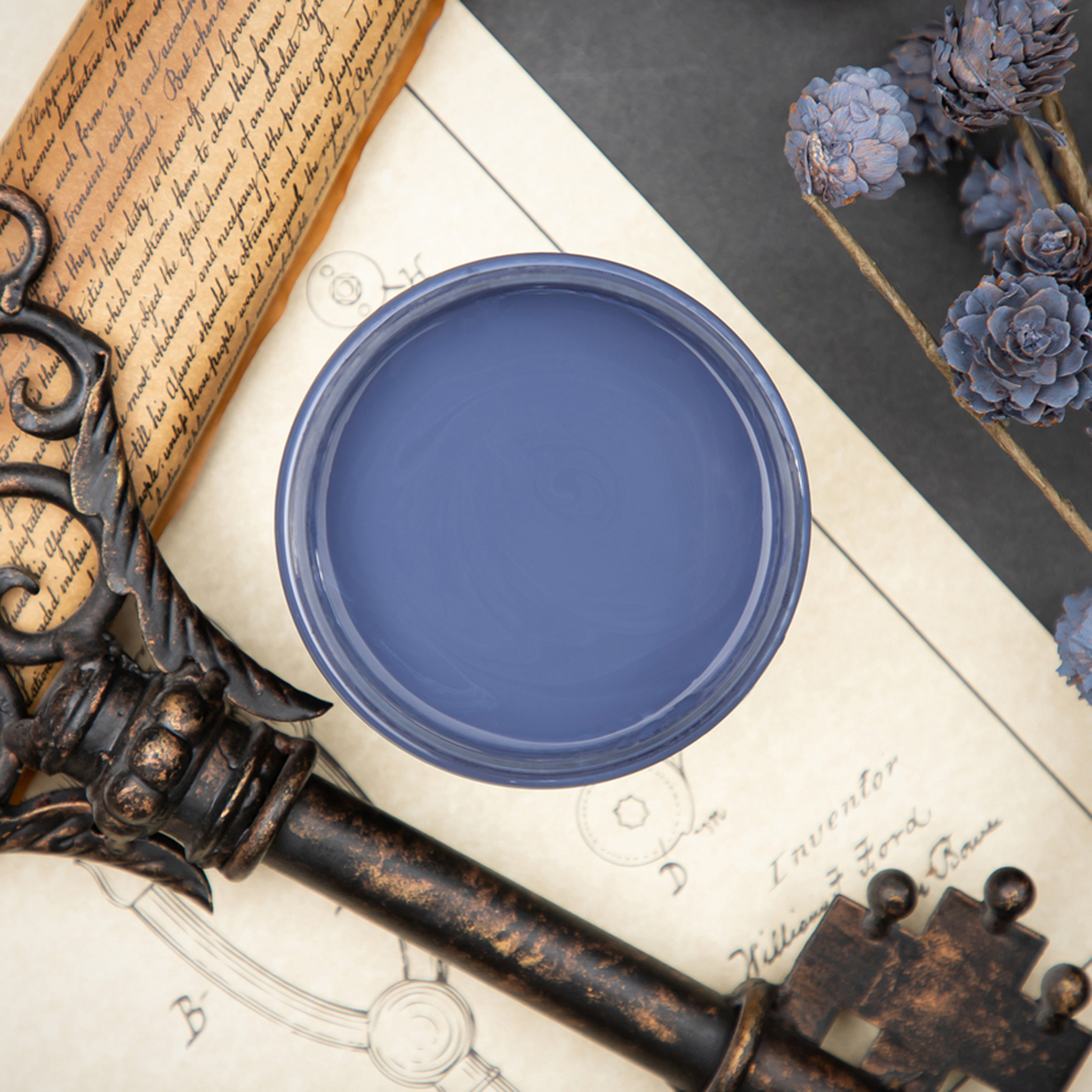 An arial view of an open container of Dixie Belle Paint Company’s Yankee Blue Chalk Mineral Paint is surrounded by a vintage key and blue-painted pine cones.
